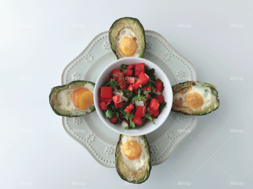 Breakfast Time Shots - flat lay of eggs baked in avocado halves arranged around pico de gallo in white bowl on white plate, white background
