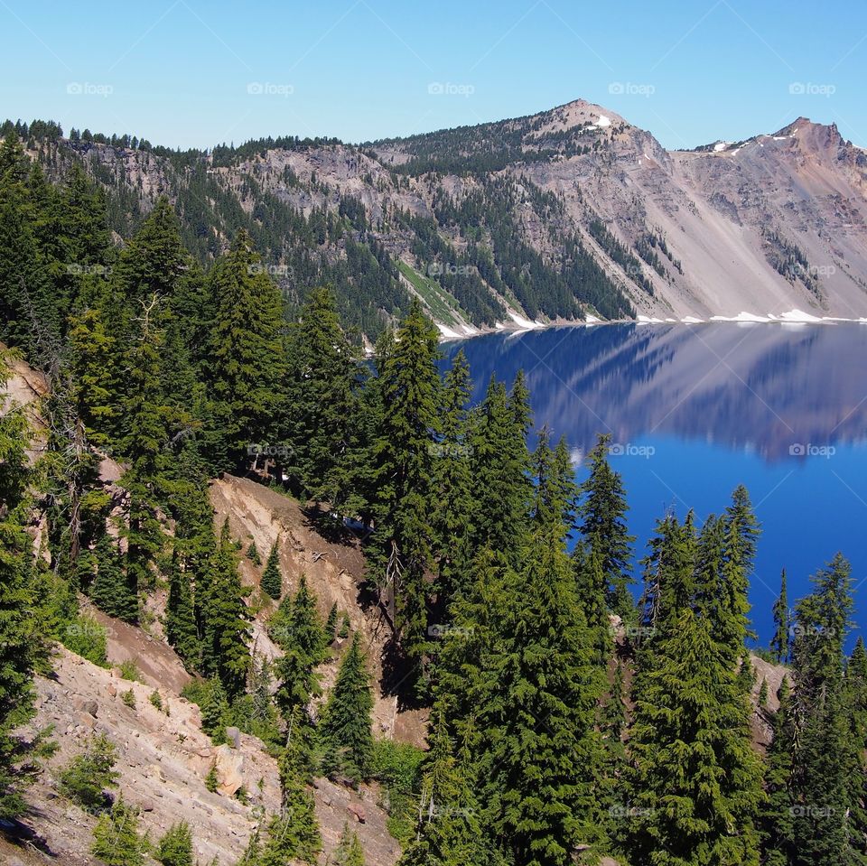 The jagged rim reflecting into the rich blue waters of Crater Lake in Southern Oregon on a beautiful summer morning with perfect clear blue skies. 