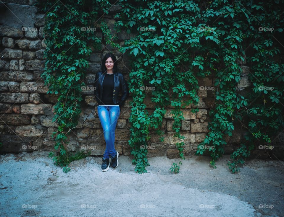 Beautiful woman in casual clothing standing near foliage wall 