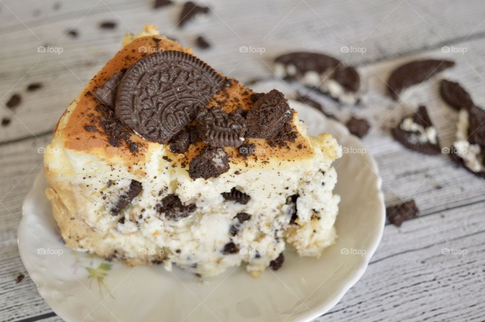 Oreo cookie cheesecake on a white plate with a white rustic background and cookie crumbles in the background