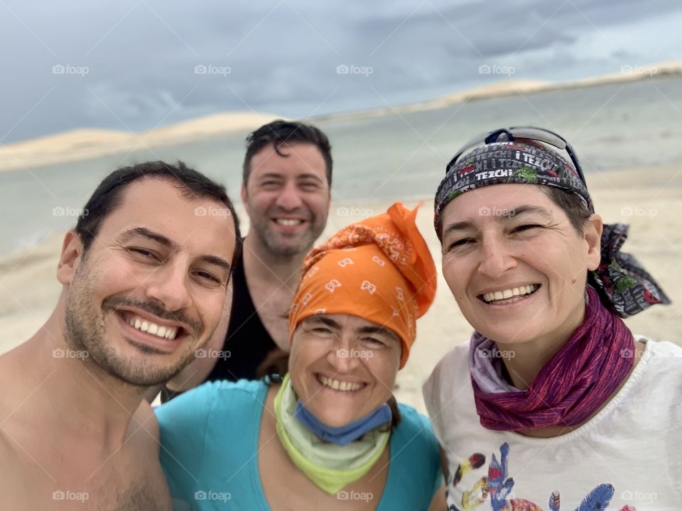 Four friends smiling against lake and dunes view 