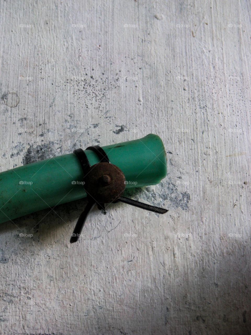 a piece of green pipe tied with black wire to a worn wooden surface