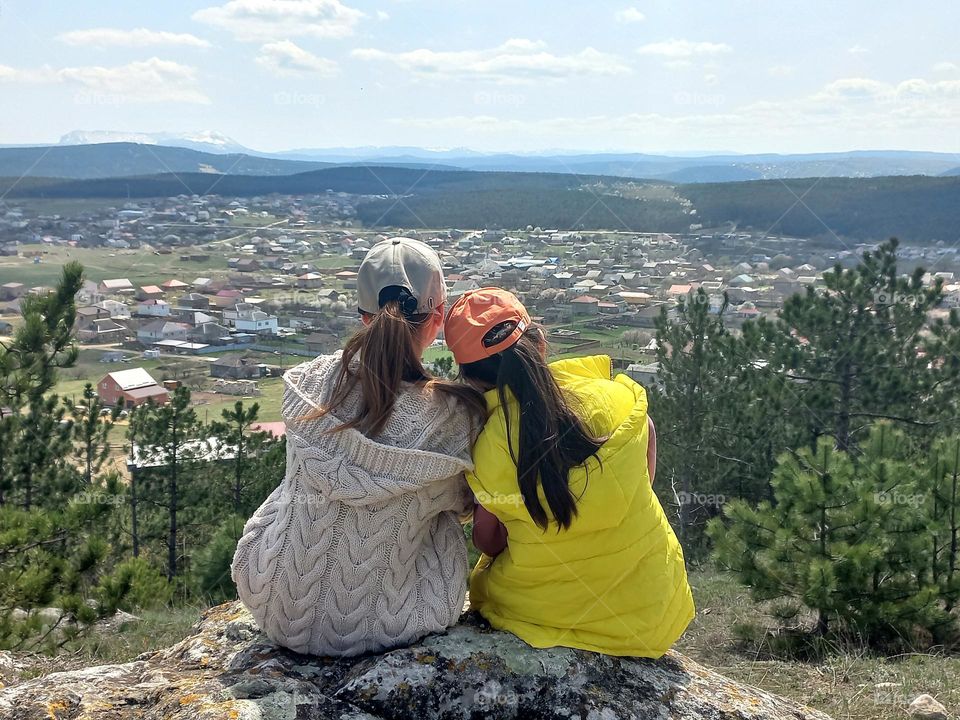 outdoor recreation, two girls sitting on a high rock and admiring the nature around.