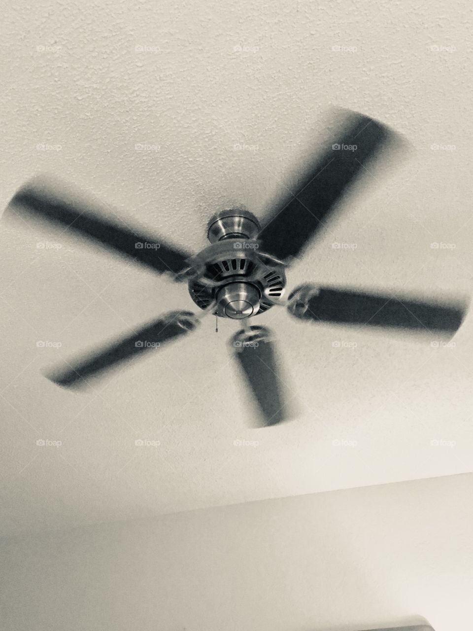 Black and white photo of a ceiling fan with blurred blades. 