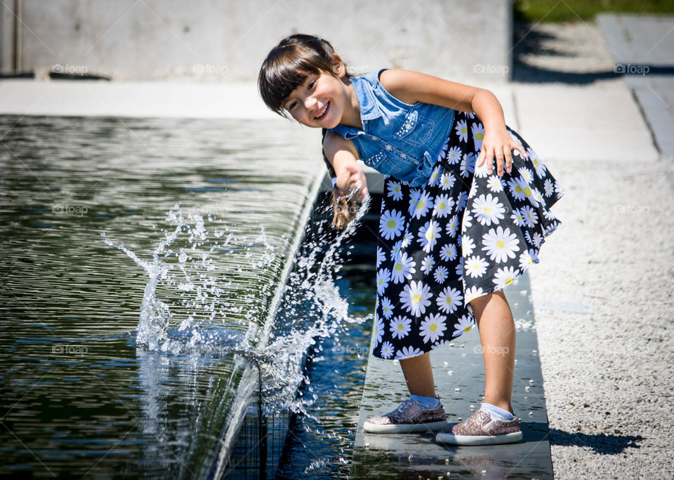 Little girl is playing with water from fountain