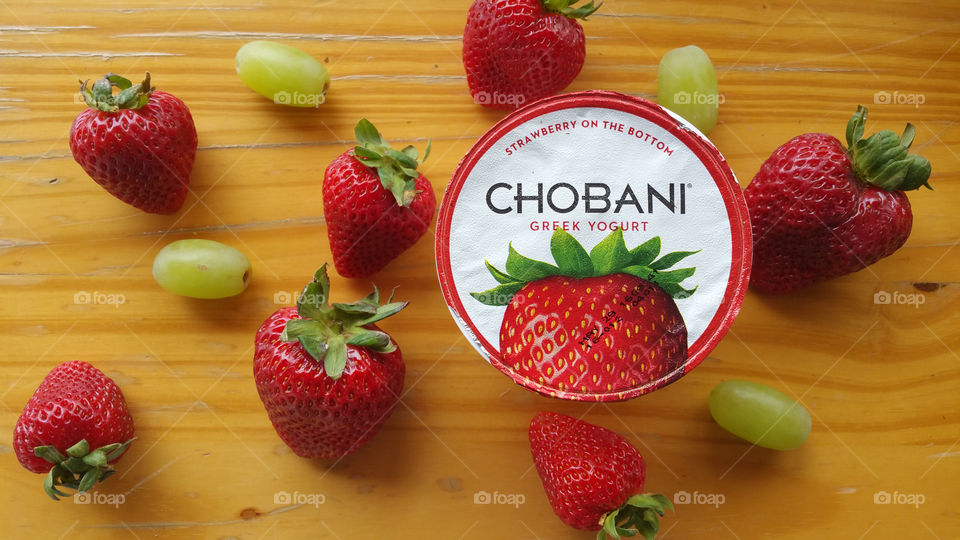 Chobani Greek yogurt strawberry flavor with strawberries and grapes with a wooden background