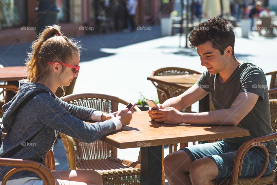 Young woman and man sitting in pavement cafe a the table talking and using mobile phones