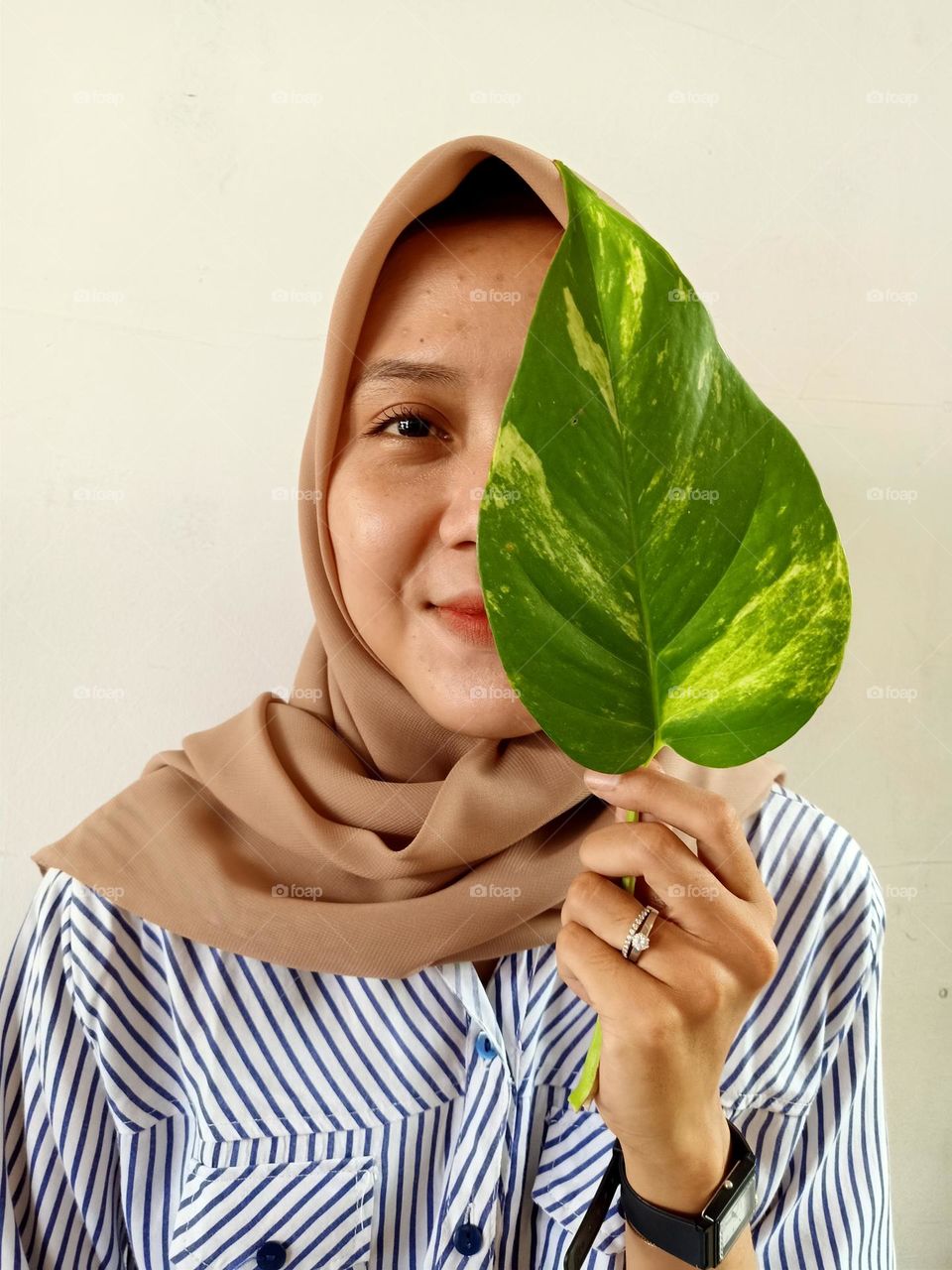 Woman holding green leaf, partially covering her face.
