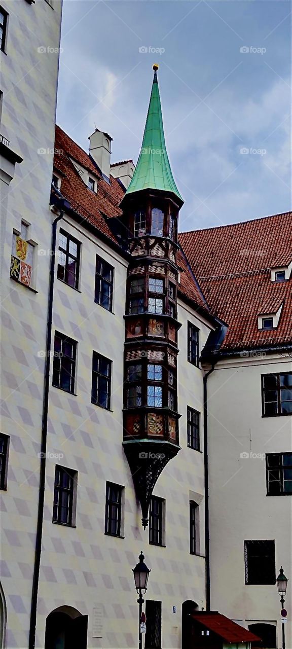 The „Alter Hof“ or old courtyard in „Munich“, capitol of „Bavaria“ has tall ceilings, a steep shingled roof and a round tower with rich ornamentation that is partially attached but ends with its own steeple rooftop. 2023. Hypnotic Productions