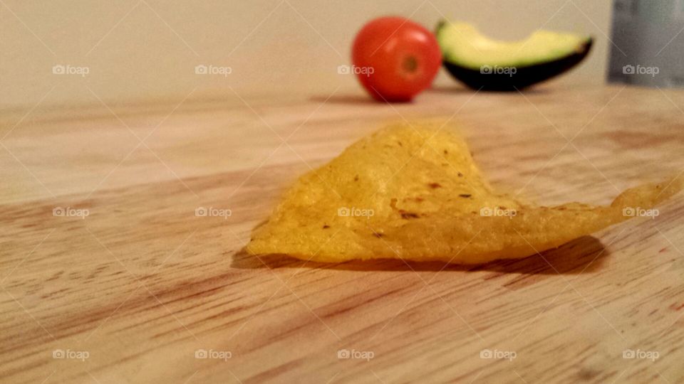 up close of tortilla chip with tomato and avocado in background