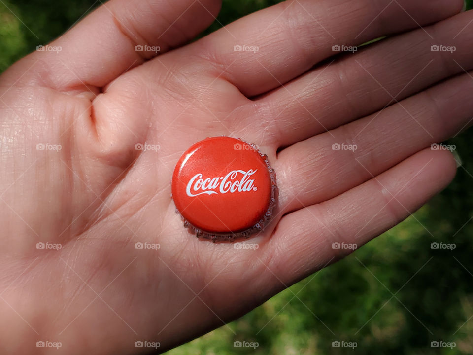 Coke cap in hand illuminated by sunlight