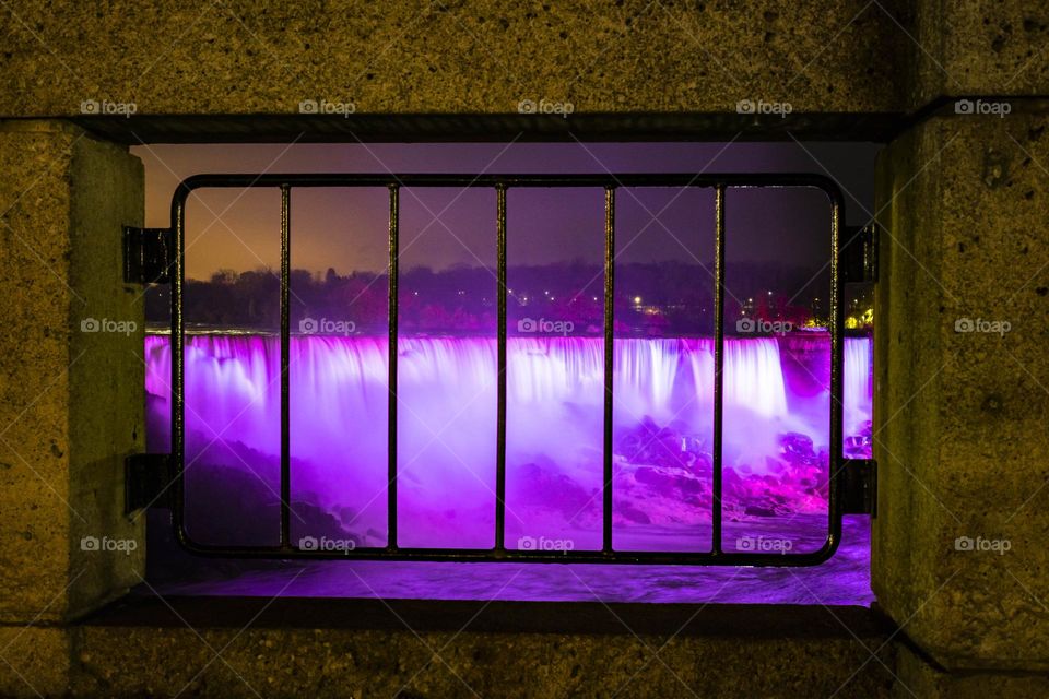 Purple lights on Niagara Falls in Canada looking through a railing 