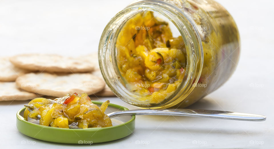 Homemade sweet mustard pickles in a jar on it's side with a spoonful on the lid and dry crackers at the side.