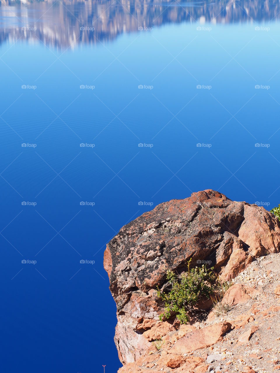 A jagged cliff over a brilliant blue Crater Lake in Southern Oregon on a beautiful summer morning. 