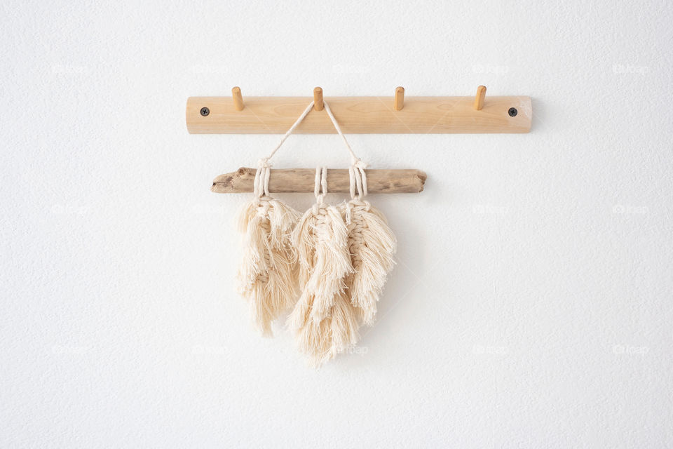 a small macrame panel on a wooden hanger on a white wall