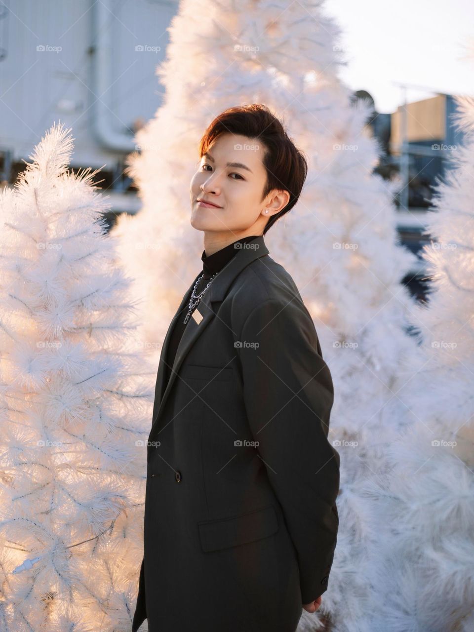 Young handsome boy from Hong Kong is smiling surrounded by many white Christmas trees 