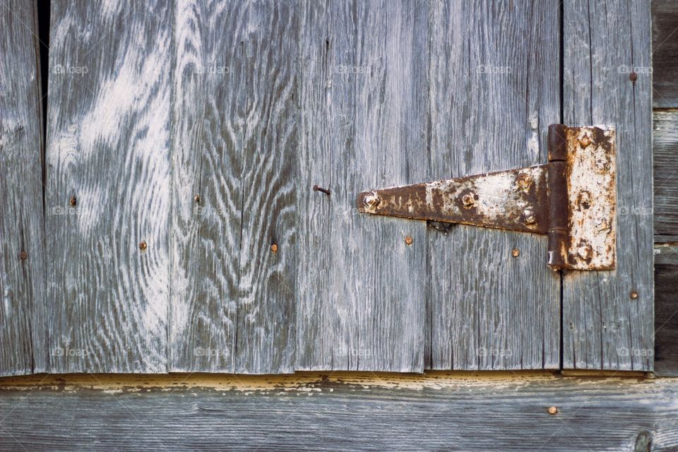 A rusty white hinge on a weathered wooden hay loft  door