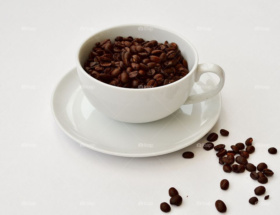 Literally, a cup of coffee. Coffee beans in a plain white china cup on a saucer with a few beans scattered alongside. 