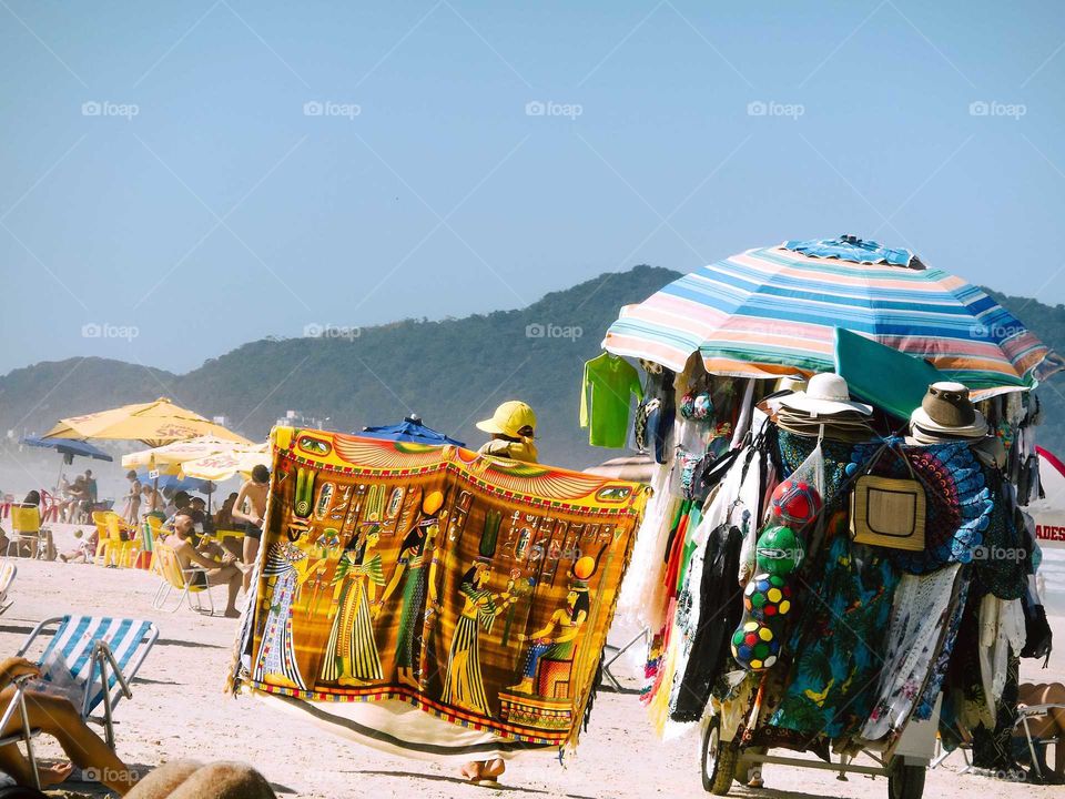 Beautiful Brazilian Beach, at Guarujá's Enseada Beach, sunny day . There's a Man with a cart, a shop cart, selling cloths, balls and umbrellas.