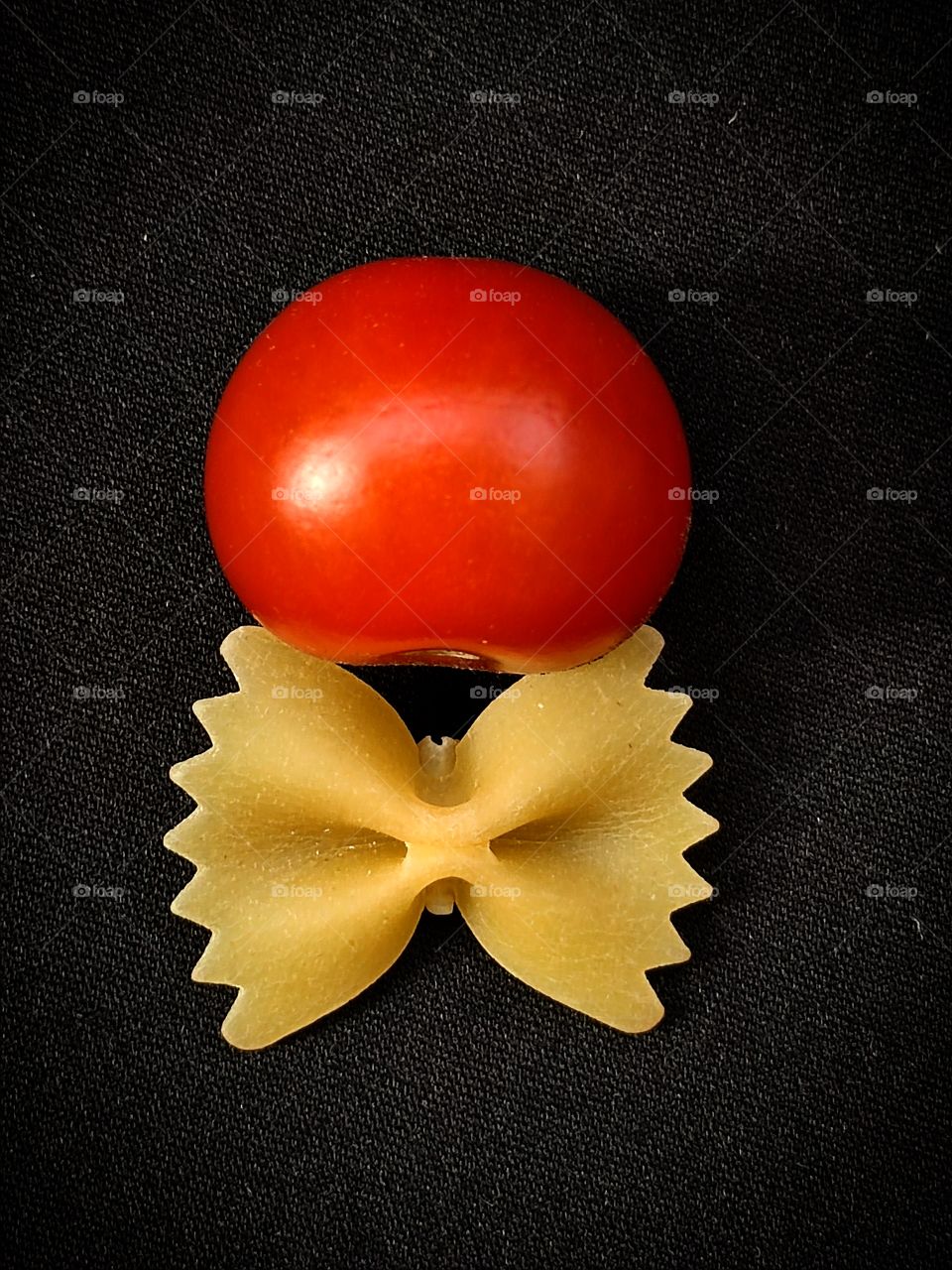 Tomato and pasta.  Food.  Association with tomato and bow tie.  Black background