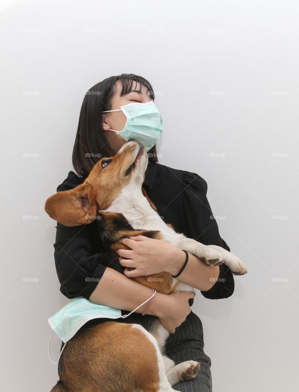 Lovely young woman hugging her cute beagle dog both wearing Covid protective mask to stay safe