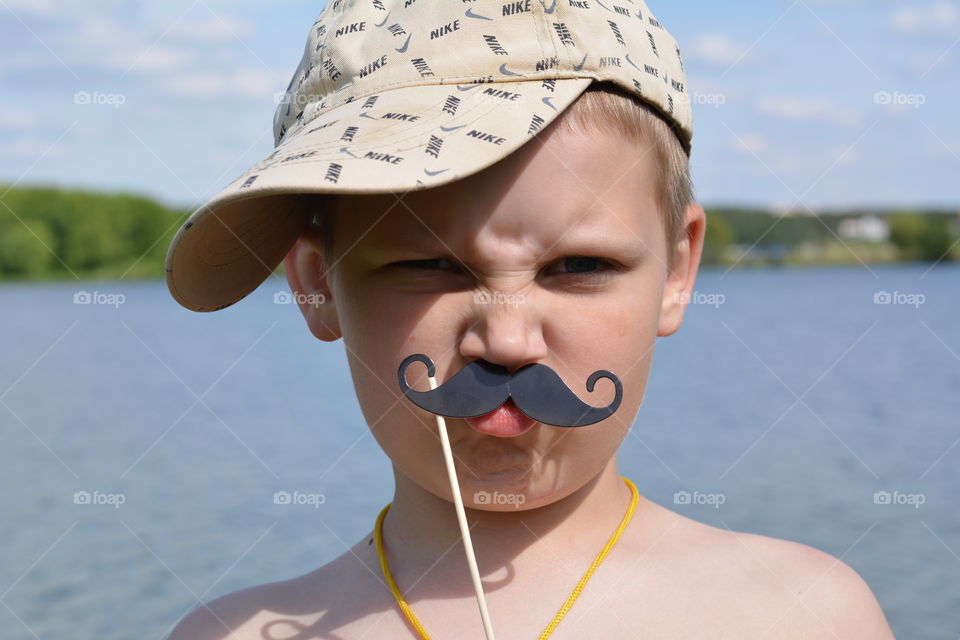 child boy with mustache funny portrait, indulge, outdoor, lake, blue sky background, summer time