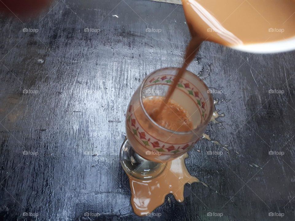 a cup of mocha coffee that was being poured but spilled over a small glass in the morning