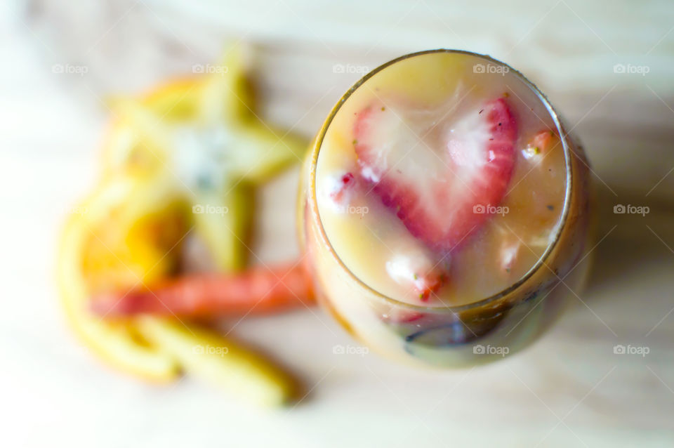 Dreamlike fresh sweet vegetable smoothie with orange, carrots carambola, star fruit, honey yogurt swirls high angle view of heart shaped strawberry on top yellow and orange Colors