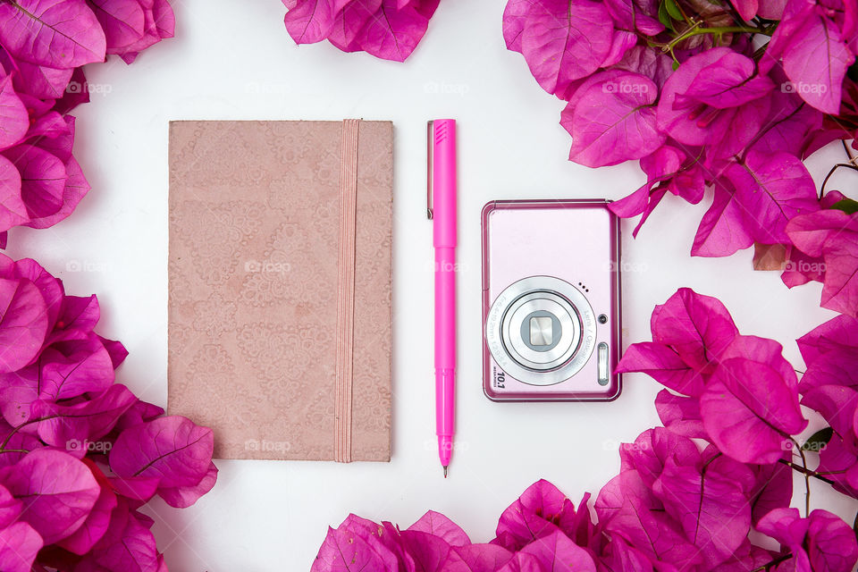 My daily routine: plan my day, and take some photos! Image of pink notebook pen and camera on white background with pink bougainvillea flowers.