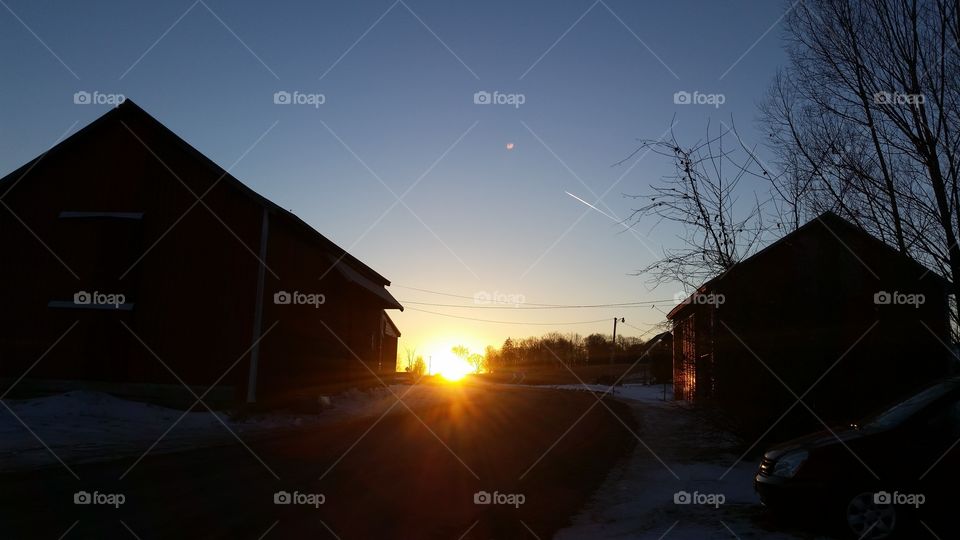 sun setting on the road between 2 barns