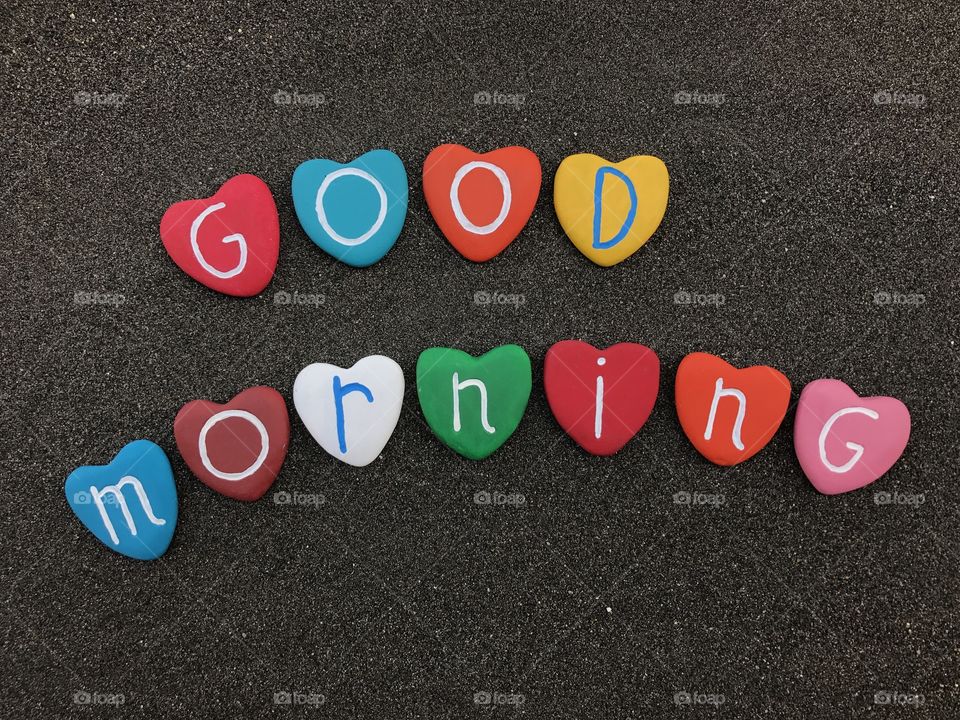 Good morning with colored heart stones over black volcanic sand