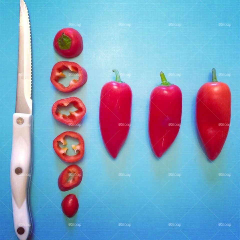 Megan Plançon . Red chili peppers on light blue background with one sliced next to chef's knife