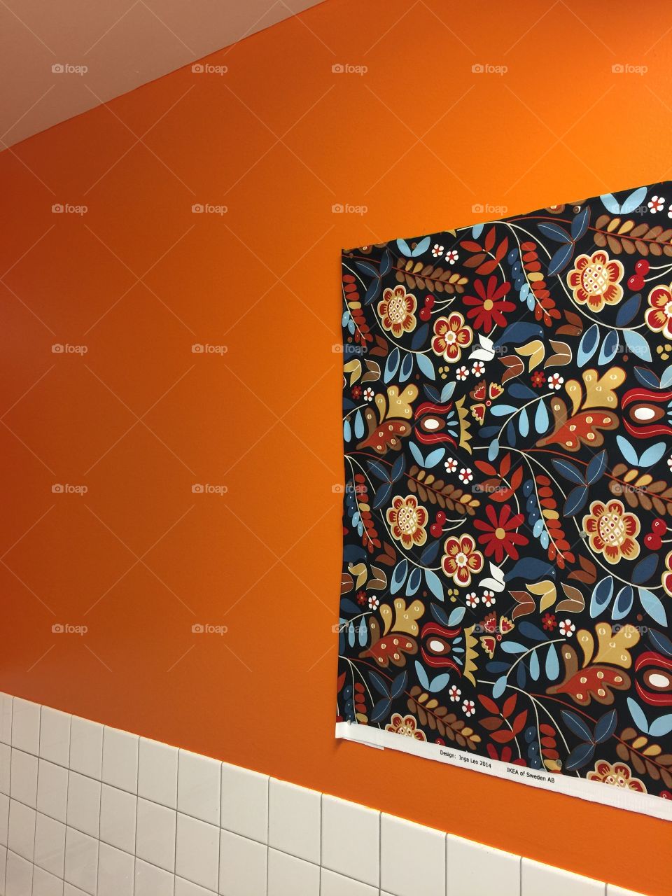 Orange wall with white tile and multi colored cloth floral tapestry