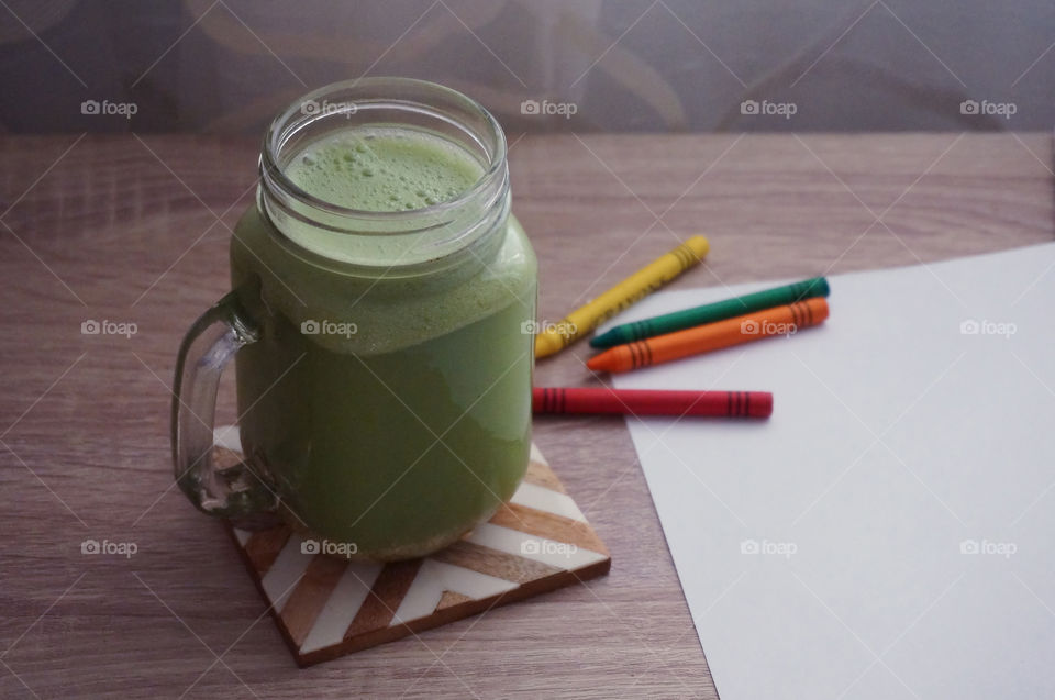 Green celery smoothie in wooden desk with colored pencils