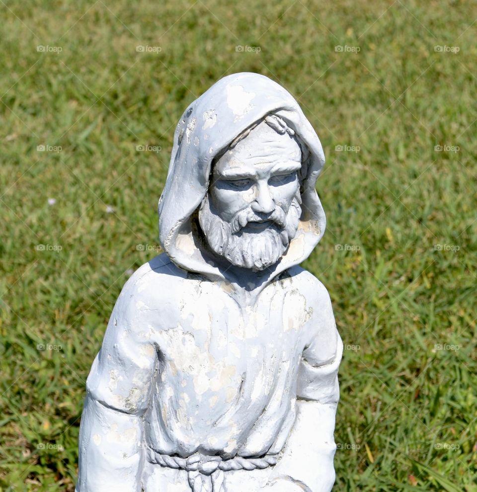 A closeup of a concrete sculpture of a man in a hooded robe with a beard and mustache 