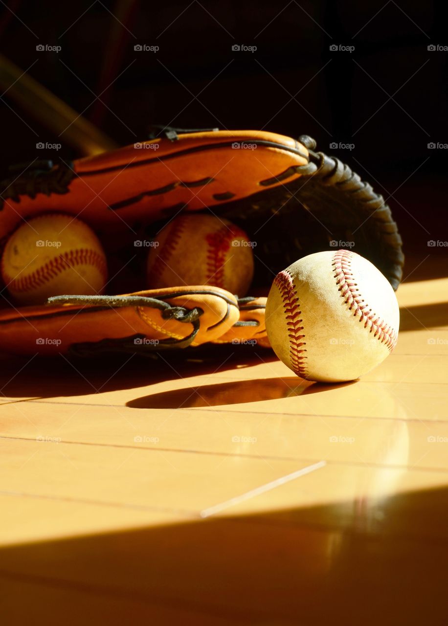 A glove and baseballs sit in the sun on a livingroom floor.