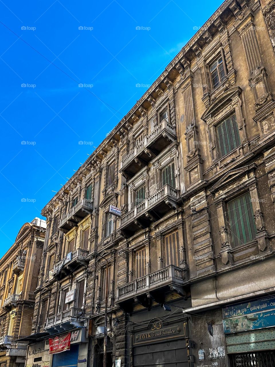 The historic architecture of Mahatet El Raml neighborhood in Alexandria, Egypt, showcasing weathered buildings with intricate balconies under a clear blue sky.