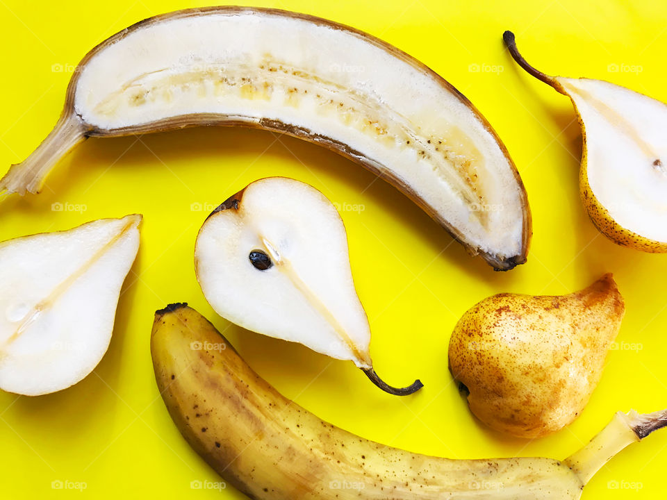 Pattern made of Slices of yellow ripe bananas and pears on yellow monochrome background 