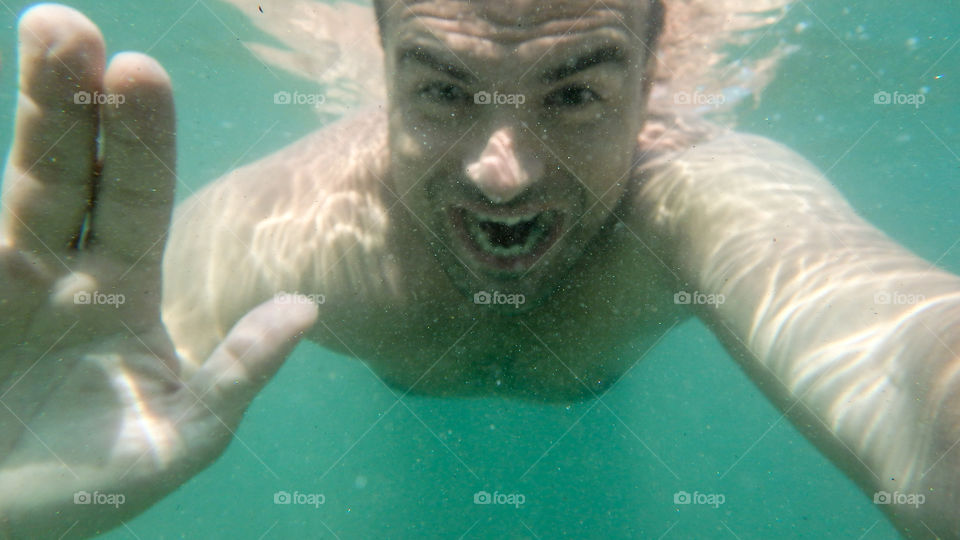 Man diving, man underwater smiling and relaxing in big blue sea