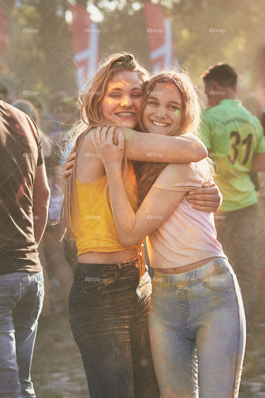 Portrait of happy smiling young girls with colorful paints on faces and clothes. Two friends spending time on holi color festival