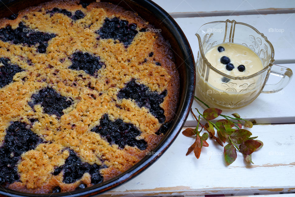 Blueberry pie and custard on a white wooden table with blueberry leaves for decoration