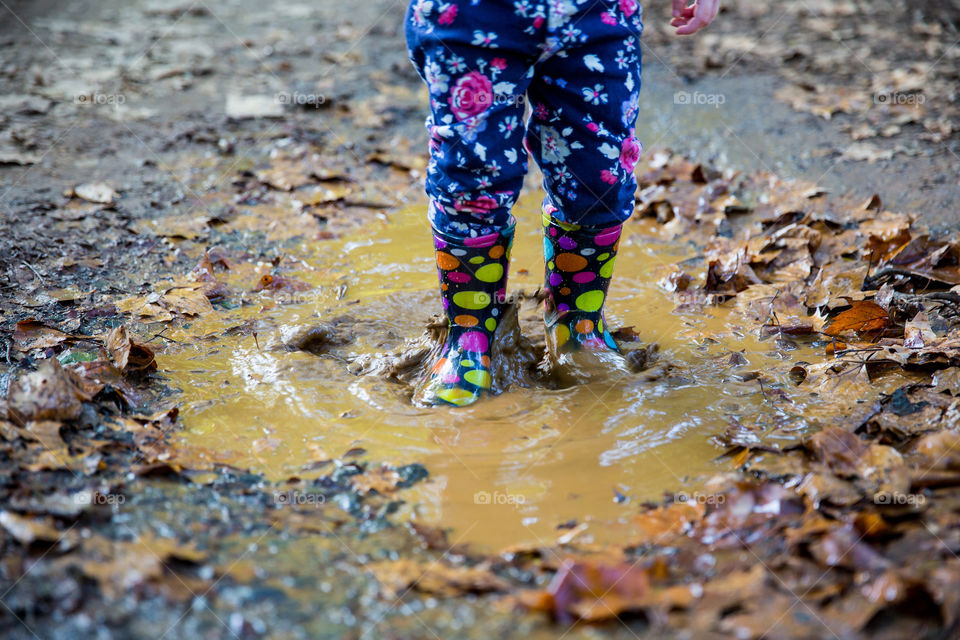 South African winter's day - muddy puddles, fallen leaves and winter rain puddles. Image of girl with water boots jumping in mud puddle in winter.