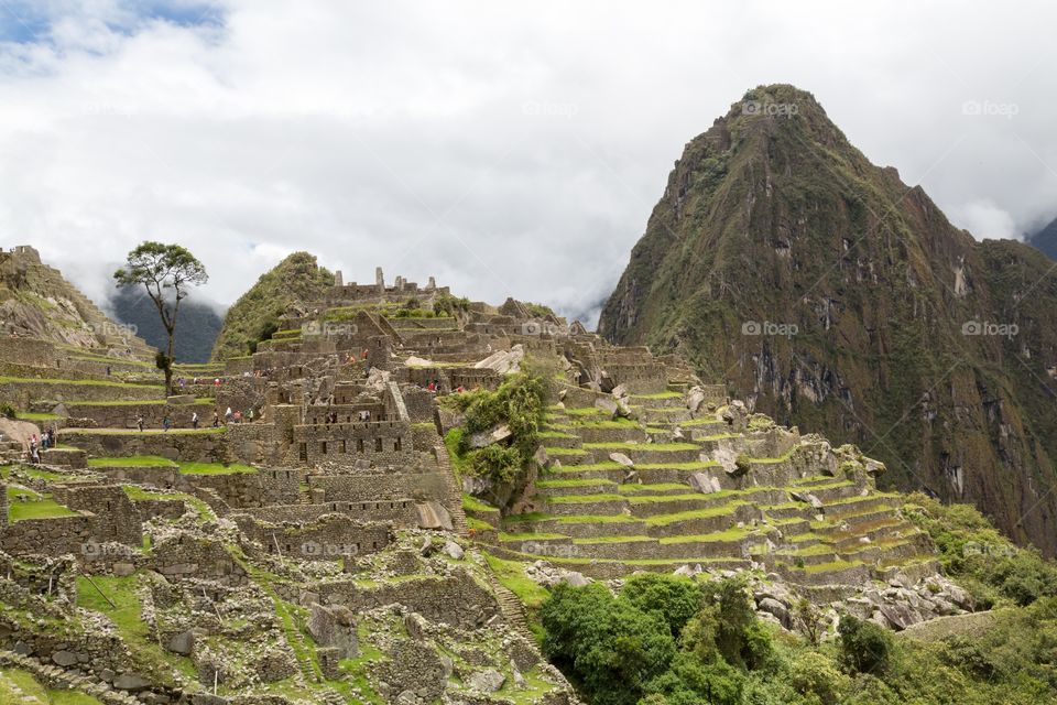 Machu Picchu ruins and terrace. Famous Machu Picchu farming terraces next to ruins. Famous mountain peak in the background. Small tourists walking 