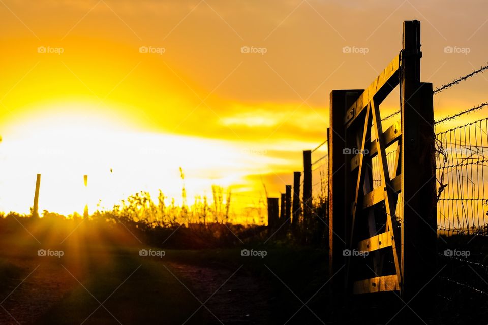 Gateway to the sun: a farm gate frames a low sunrise in a rural setting. 