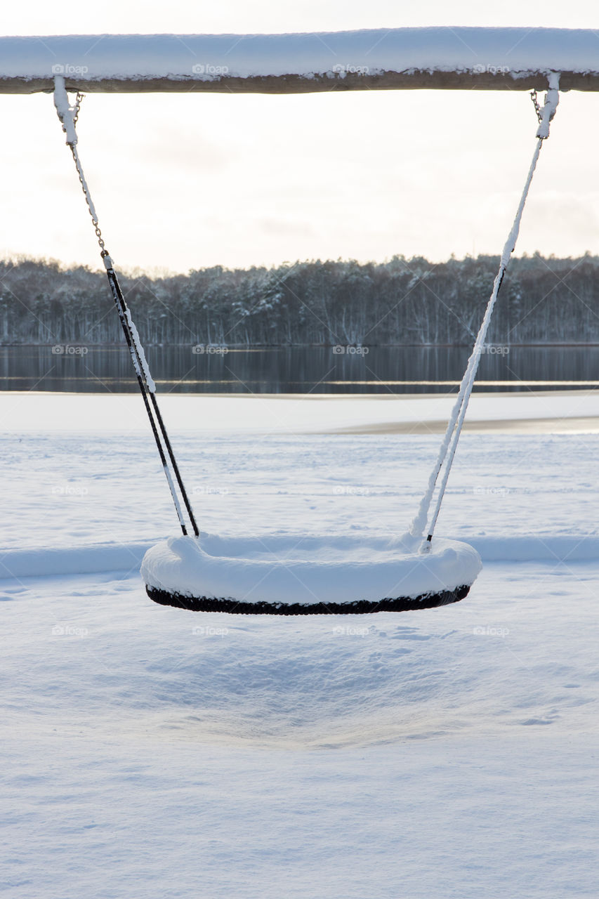 Snowy swing with a nice view of lake and forest, playground in untouched snow, winter 