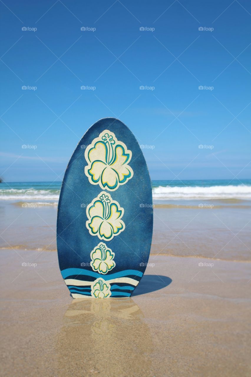Blue body board on the beach in front of the sea on a bright sunny day.