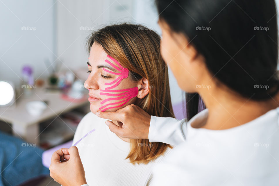 Young woman gets facial tape massage in spa beauty salon 