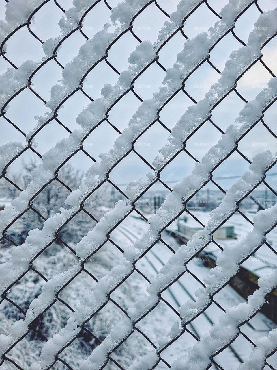 Metal fence in the form of rhombuses with snow.  Winter. Geometric shapes