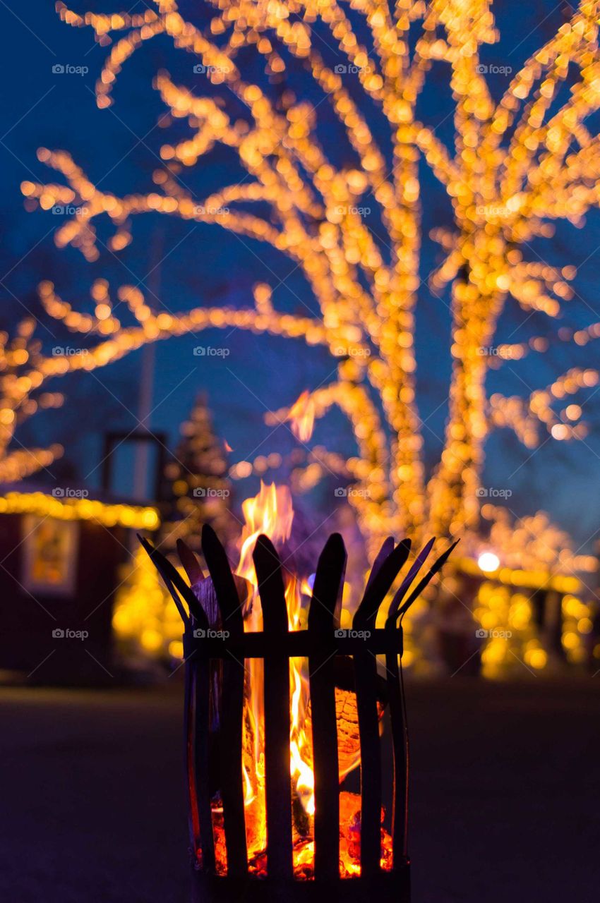 Outdoor fire at night, in front of winter lights.