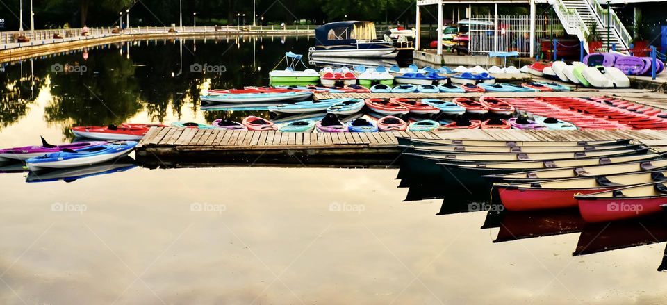 Colourful kayaks, canoes, and peddle boats tied up and waiting for peacefully in the morning sun.